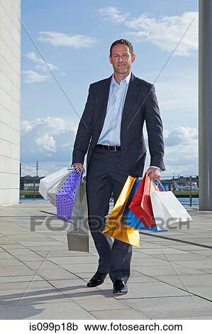 Mid adult man carrying shopping bags View Large Photo Image Stock Image - Mid adult man carrying shopping bags. Fotosearch