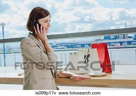 Mid adult woman on cell phone in airport View Large Photo Image Stock Photo - Mid adult woman on cell phone in airport. Fotosearch