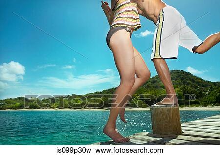 Playful couple on jetty by the ocean View Large Photo Image Stock Photo - Playful couple on jetty by the ocean. Fotosearch
