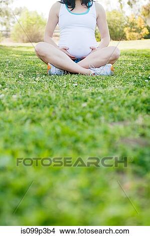Picture - Pregnant young woman sitting cross legged on grass. Fotosearch