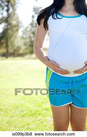 Pregnant young woman touching stomach, front view View Large Photo Image Stock Photo - Pregnant young woman touching stomach, front view. Fotosearch