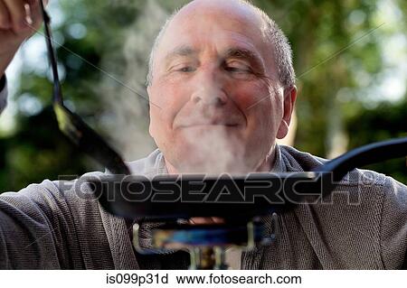Stock Image - Senior man cooking on camping stove. Fotosearch