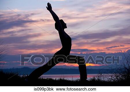 Stock Image - Silhouette of woman in warrior yoga pose at sunset. Fotosearch
