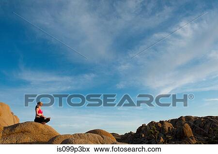 Stock Photo - Woman meditating on desert rocks. Fotosearch