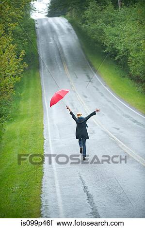 Stock Image - Woman on empty road with red umbrella. Fotosearch