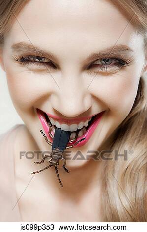 Stock Image - Young woman biting plastic beetle. Fotosearch