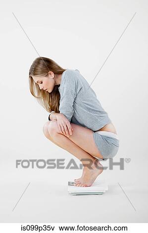 Young woman crouching on weight scales View Large Photo Image Stock Photo - Young woman crouching on weight scales. Fotosearch