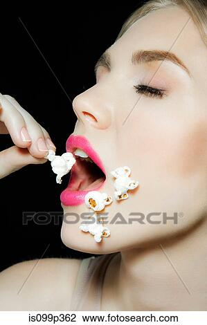 Stock Image - Young woman eating popcorn. Fotosearch