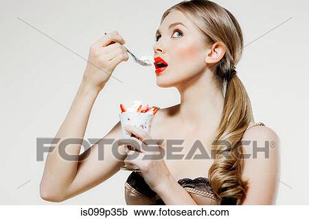 Stock Image - Young woman eating strawberries and cream. Fotosearch