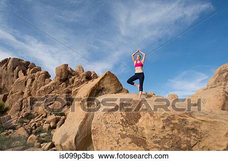 Stock Photograph - Young woman in tree pose on desert rocks. Fotosearch