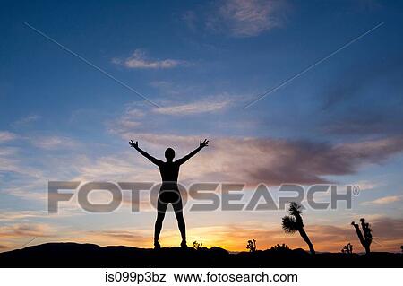 Stock Photo - Young woman standing in desert with arms open, silhouette. Fotosearch