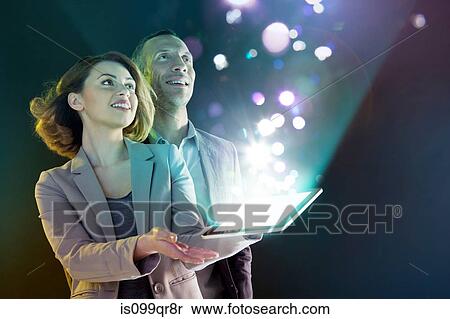Stock Photography - Businesspeople looking at lights coming from digital tablet. Fotosearch