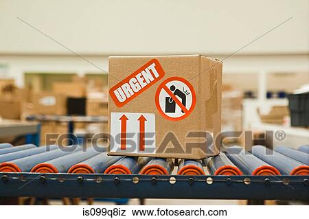 Stock Photo - Cardboard box with warning stickers on conveyor belt. Fotosearch