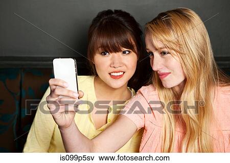 Stock Photo - Female friends photographing themselves on smartphone. Fotosearch