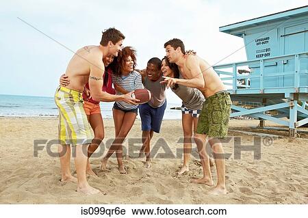 Stock Image - Friends on beach playing rugby. Fotosearch