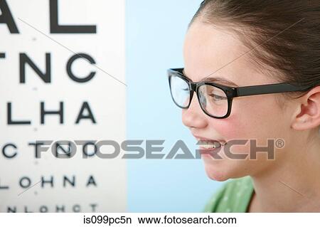 Girl wearing glasses with eye chart in background View Large Photo Image Picture - Girl wearing glasses with eye chart in background. Fotosearch