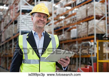 Stock Photography - Man holding digital tablet in warehouse, portrait. Fotosearch