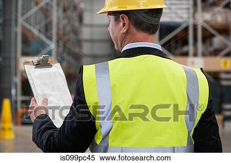 Stock Photography - Man in warehouse holding clipboard, rear view. Fotosearch