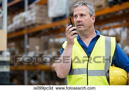 Stock Image - Man on walkie talkie in warehouse. Fotosearch
