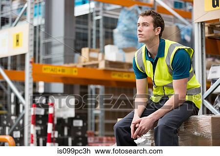 Stock Image - Man sitting on cardboard box in warehouse. Fotosearch