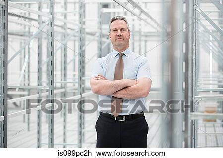 Stock Image - Man with arms folded in empty warehouse, portrait. Fotosearch