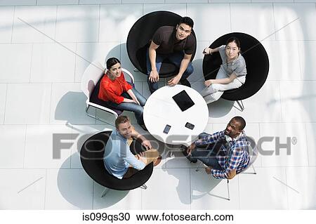Stock Image - Overhead view of colleagues in meeting, looking up at camera. Fotosearch