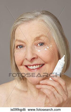 Stock Image - Senior woman applying eye cream. Fotosearch