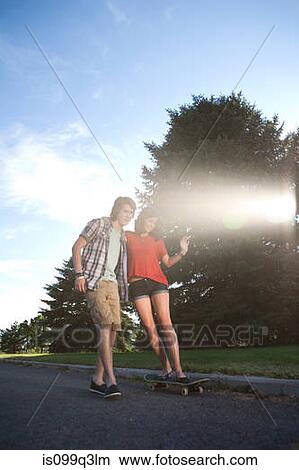 Teenage boy helping girlfriend ride skateboard View Large Photo Image Picture - Teenage boy helping girlfriend ride skateboard. Fotosearch