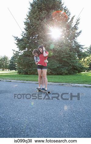 Stock Image - Teenage boy helping girlfriend ride skateboard. Fotosearch