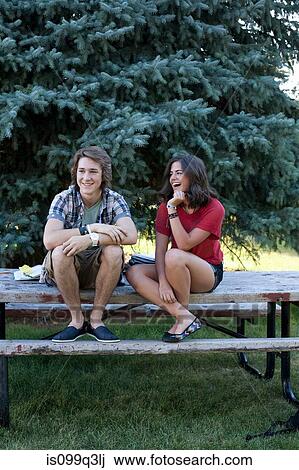 Stock Image - Teenage couple sitting on picnic table in park. Fotosearch