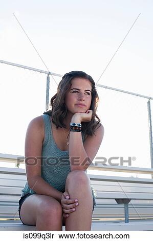 Stock Photography - Teenage girl sitting on bleachers with hand on chin, portrait. Fotosearch