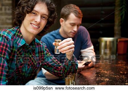 Two men at bar, one holding shot glass View Large Photo Image Picture - Two men at bar, one holding shot glass. Fotosearch