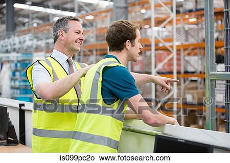 Two men in warehouse, one pointing View Large Photo Image Picture - Two men in warehouse, one pointing. Fotosearch