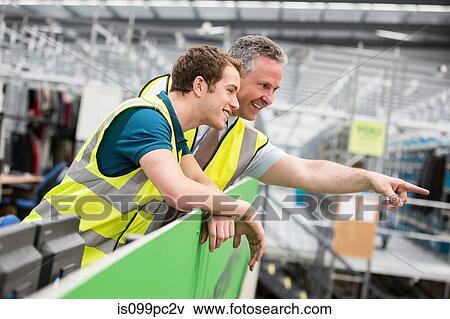 Two men in warehouse, one pointing View Large Photo Image Stock Photo - Two men in warehouse, one pointing. Fotosearch