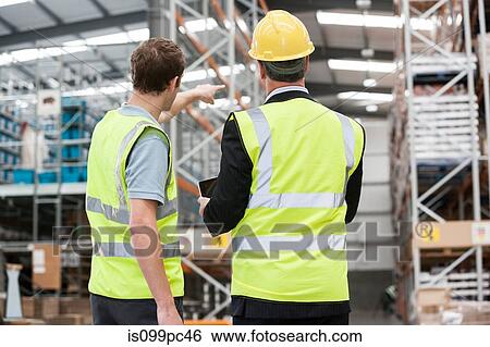 Two men in warehouse, one pointing View Large Photo Image Stock Photograph - Two men in warehouse, one pointing. Fotosearch