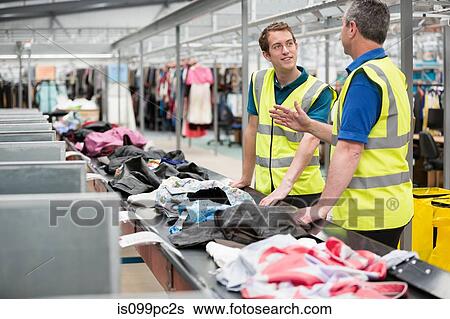 Stock Photograph - Two men sorting clothes on conveyor belt in warehouse. Fotosearch