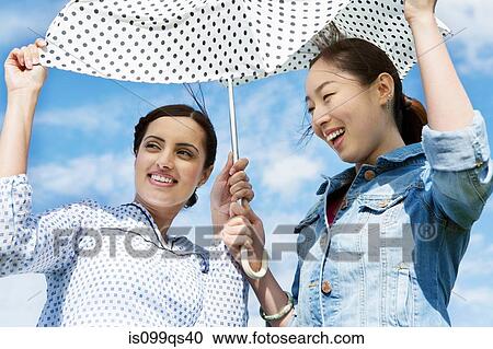 Stock Image - Two young women outdoors with parasol. Fotosearch