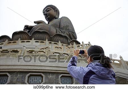 Stock Image - Woman taking photograph of tian tan buddha, hong kong, china. Fotosearch