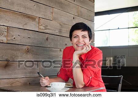 Stock Image - Woman wearing red shirt sitting in cafe, portrait. Fotosearch