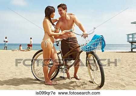 Stock Image - Young couple on beach with bicycle. Fotosearch