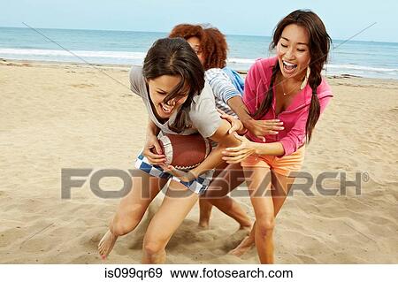 Stock Photo - Young female friends playing rugby on beach. Fotosearch