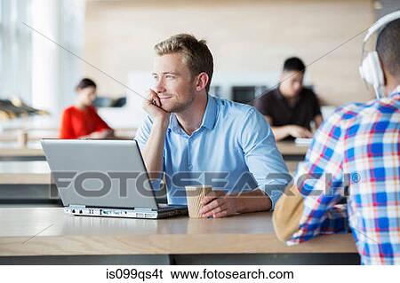 Stock Photograph - Young man in break room with laptop. Fotosearch