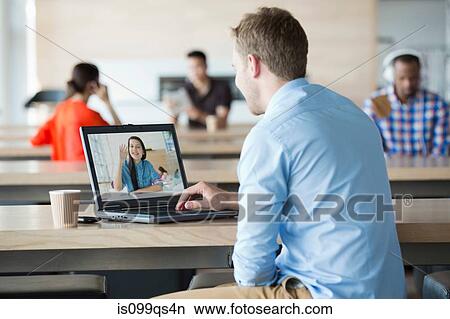 Picture - Young man using laptop to have video call with girlfriend. Fotosearch