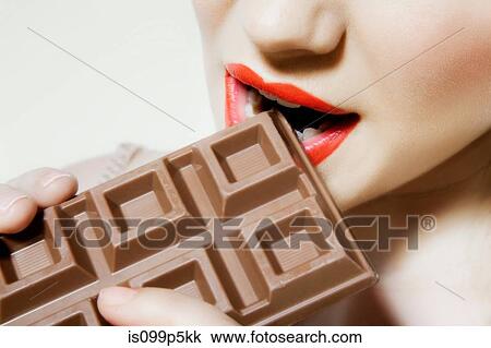 Stock Image - Young woman biting chocolate, close up. Fotosearch
