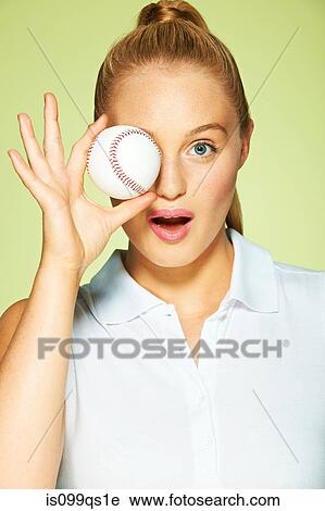 Stock Image - Young woman holding baseball in front of eye. Fotosearch