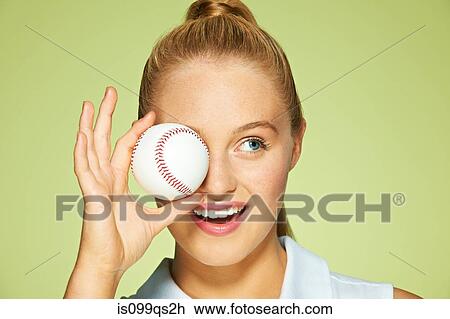 Stock Image - Young woman holding baseball in front of eye. Fotosearch
