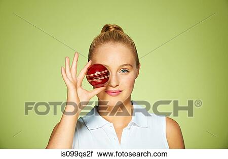 Stock Image - Young woman holding cricket ball over her eye. Fotosearch