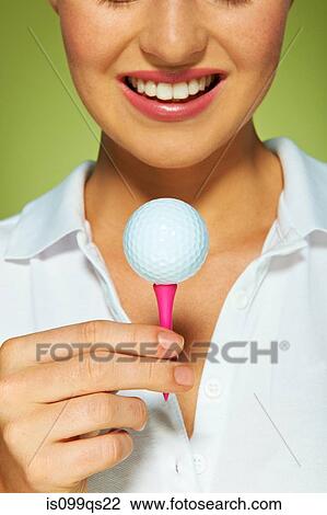Stock Image - Young woman holding golf ball and tee. Fotosearch