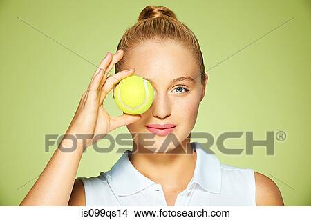 Picture - Young woman holding tennis ball over her eye. Fotosearch