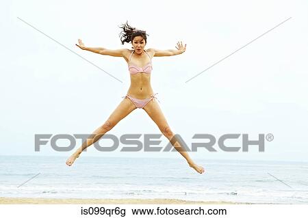 Young woman in bikini doing star jump on beach View Large Photo Image Stock Image - Young woman in bikini doing star jump on beach. Fotosearch